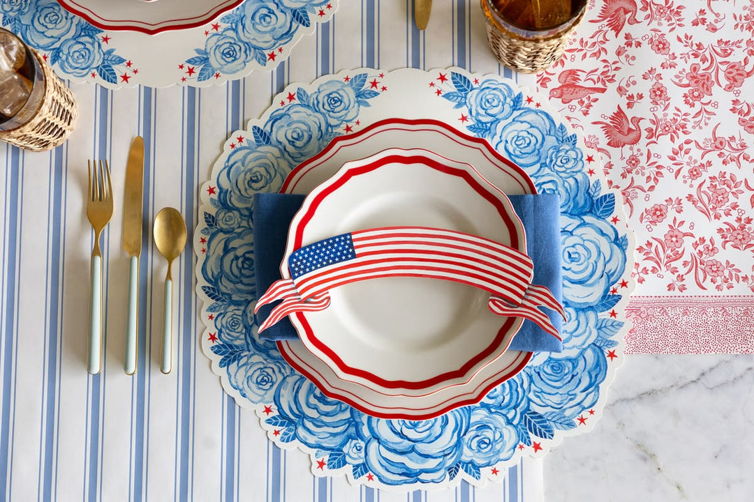 Table setting with decorative plates featuring American flag designs on a striped tablecloth.