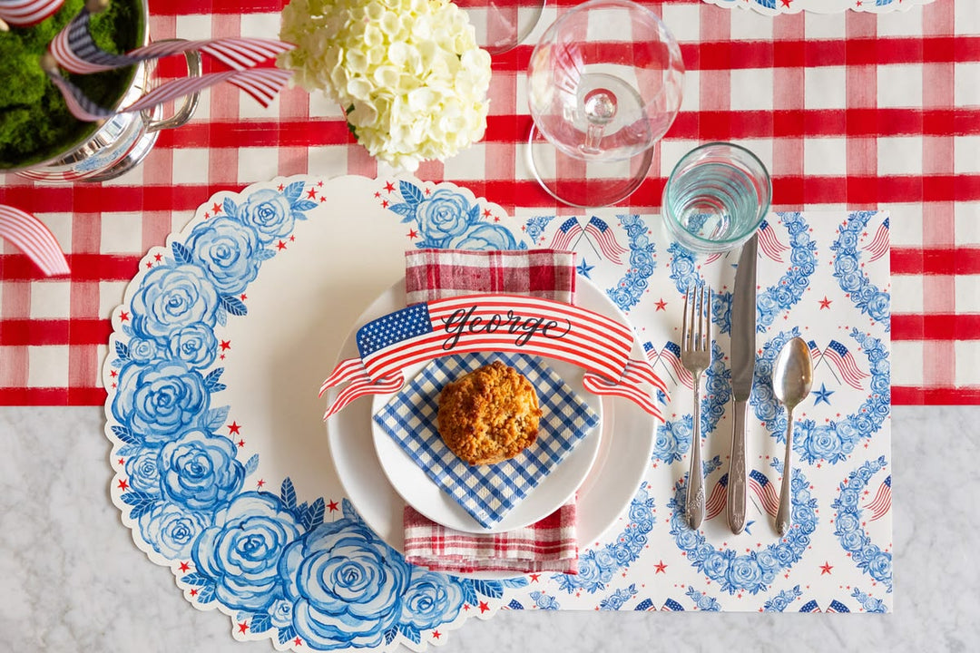 Dinner table setting with floral placemat, American flag napkin, and appetizer on a red and white checkered tablecloth.