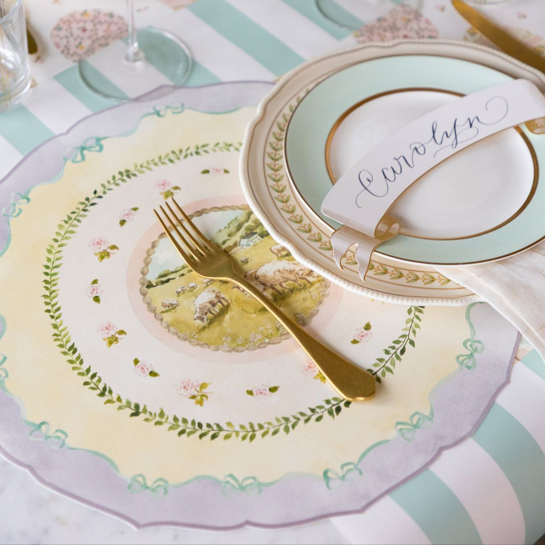 Decorative table setting with plates, cutlery, and a name card on a striped tablecloth.
