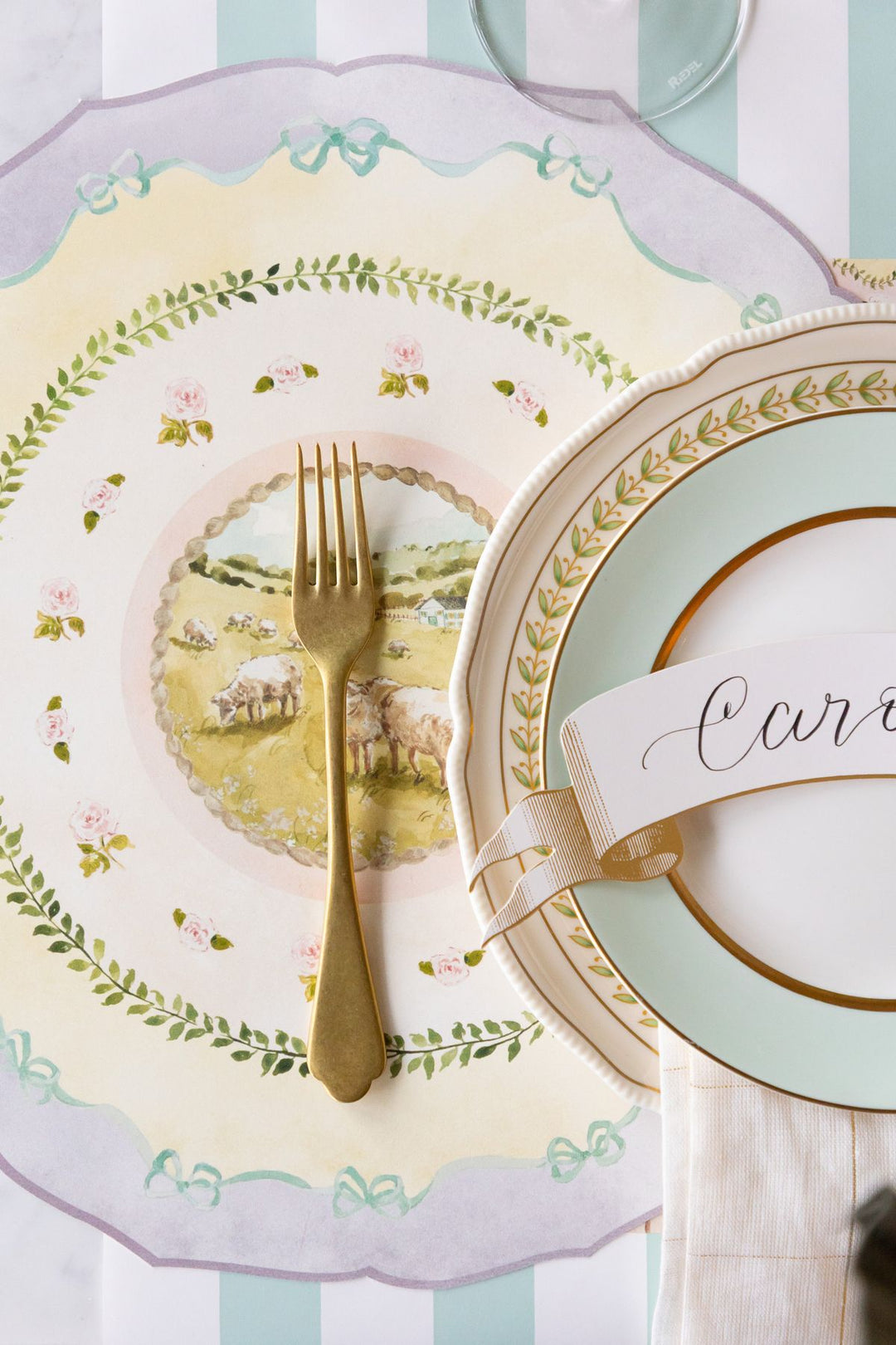 Decorative plate with pastoral scene, gold fork, and ribbon with text on a striped background