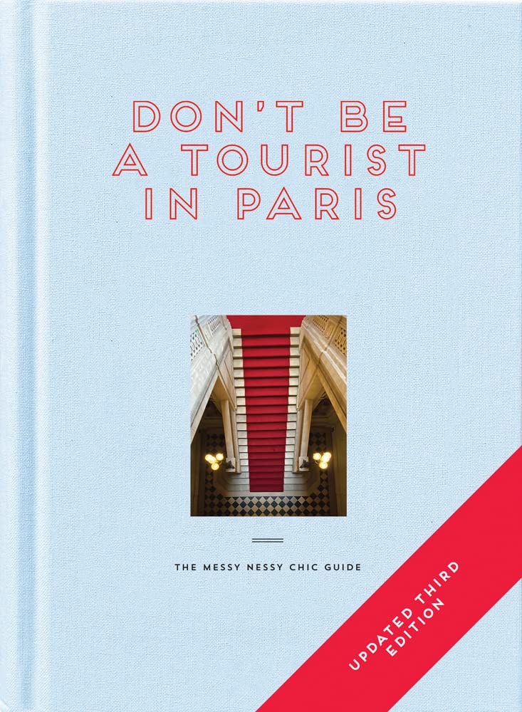 Book cover of 'Don't Be a Tourist in Paris' with a light blue background and red text.