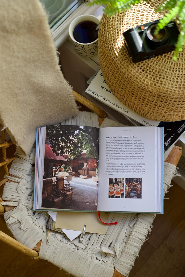 Open book on a textured surface with a cup of coffee and camera in the background