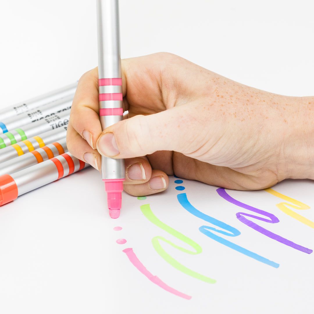 Hand holding a pink marker with colorful lines on paper