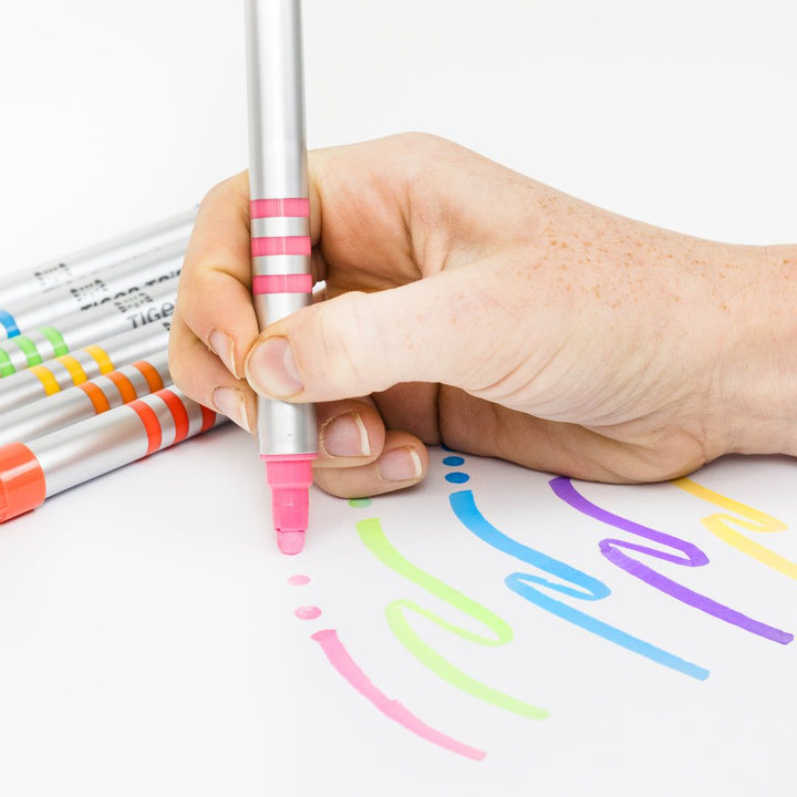 Hand holding a pink marker with colorful lines on paper