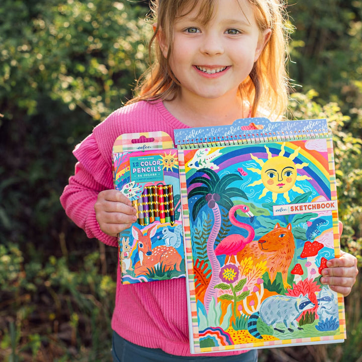 Child holding a colorful sketchbook and coloring book set outdoors