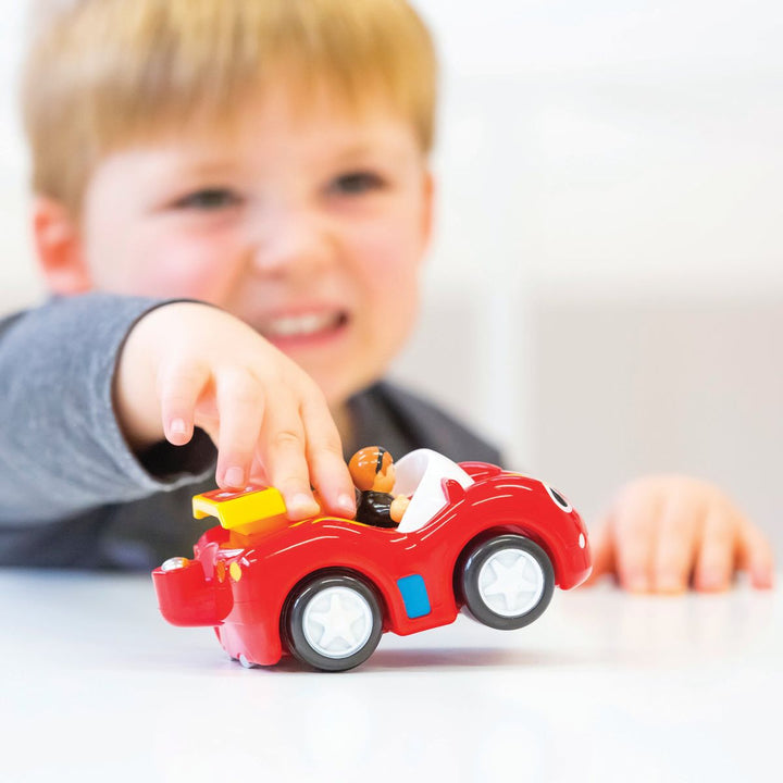 Child playing with a red toy car on a white surface