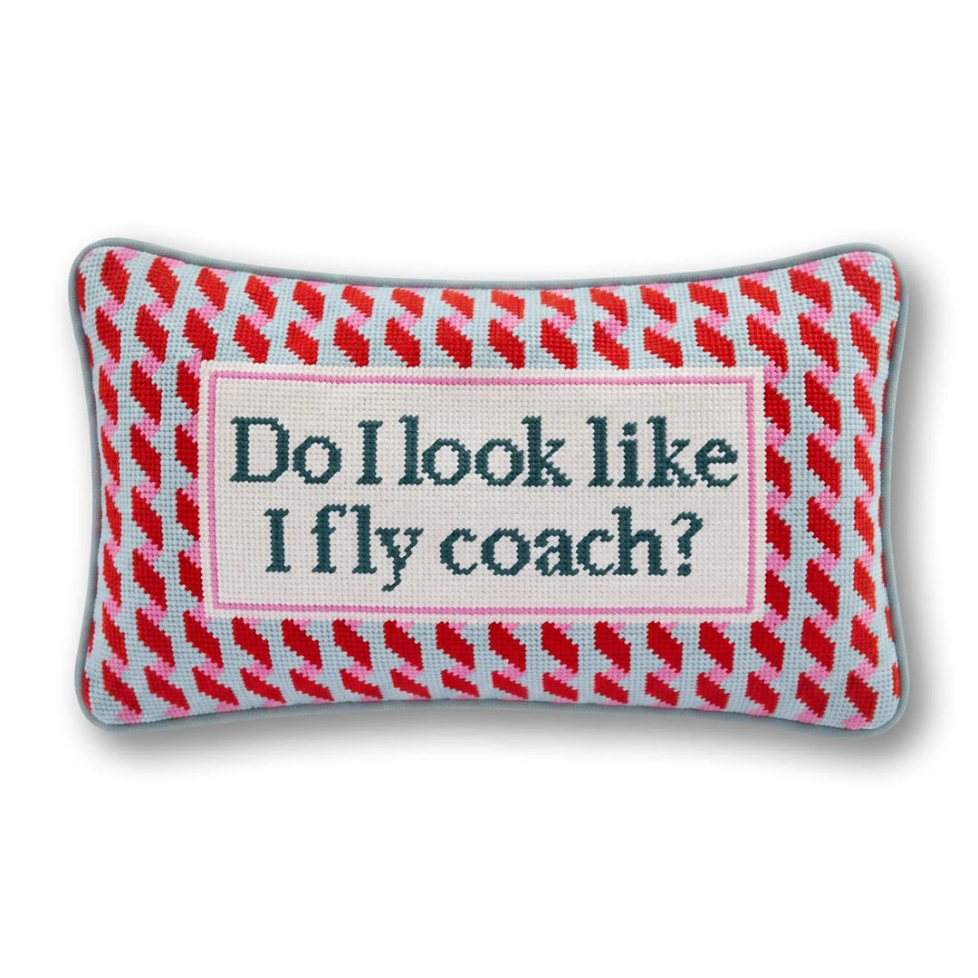 A rectangular decorative pillow with a red and pink patterned border and a central cream panel reading 'Do I look like I fly coach?' in navy lettering, shown on a white background.