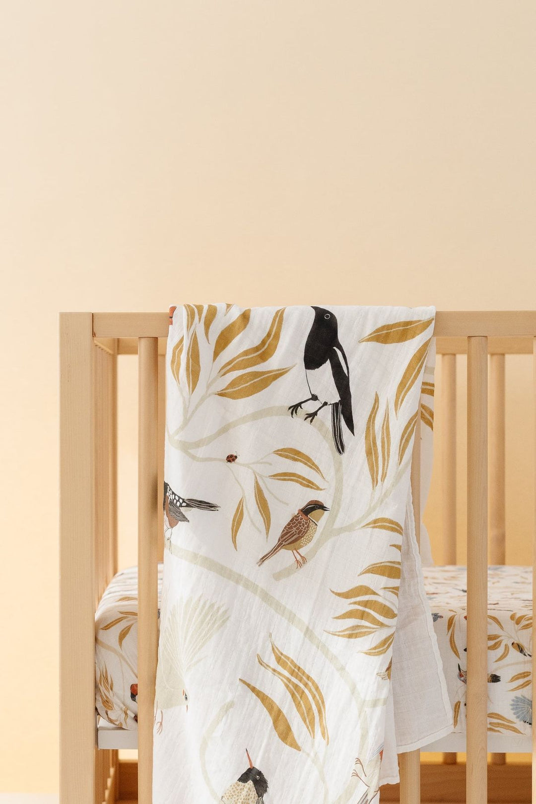 Crib with a white blanket featuring bird and leaf patterns on a beige background