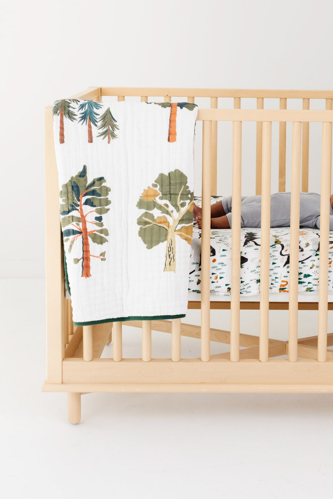 Nursery crib with a forest-themed blanket and bedding set on a white background