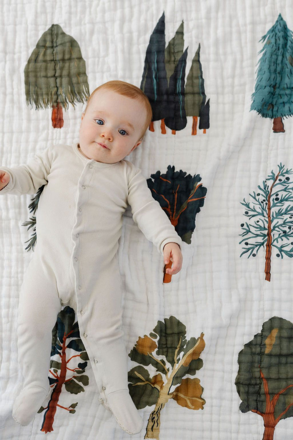 Baby lying on a forest-themed blanket with trees and animals.