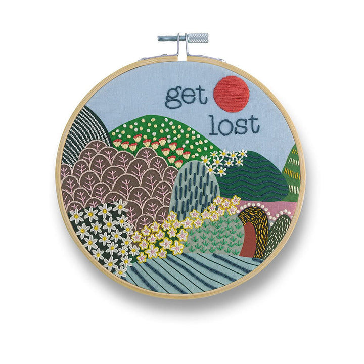 Embroidery hoop with a scenic design and 'get lost' text on a white background