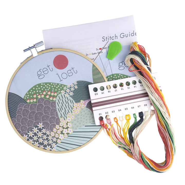 Embroidery hoop with 'get lost' text, colorful threads, and a stitch guide on a white background