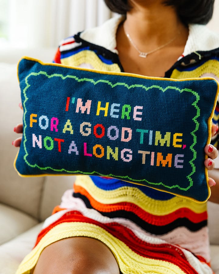 Person holding a colorful pillow with text 'I'm here for a good time, not a long time' against a neutral background.