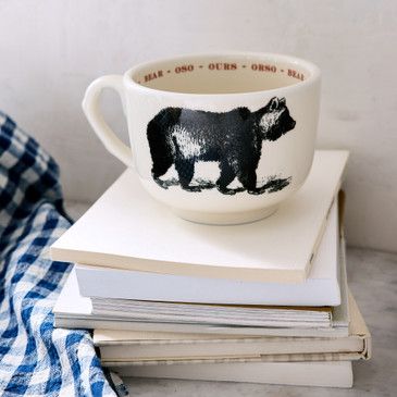 White mug with bear design on a stack of books, blue checkered towel nearby