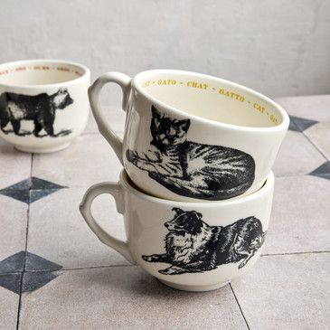 Set of three ceramic mugs with black and white illustrations of dogs on a tiled floor.