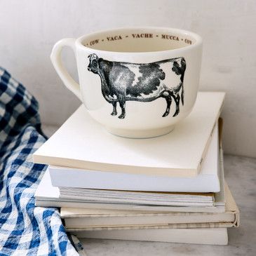 Cup with cow design on a stack of books next to a checkered cloth