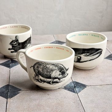 Three ceramic mugs with animal illustrations on a tiled floor.
