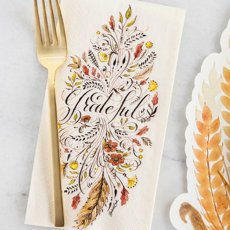 Decorative napkin with floral design and 'Blessful' text, paired with a gold fork on a light background.