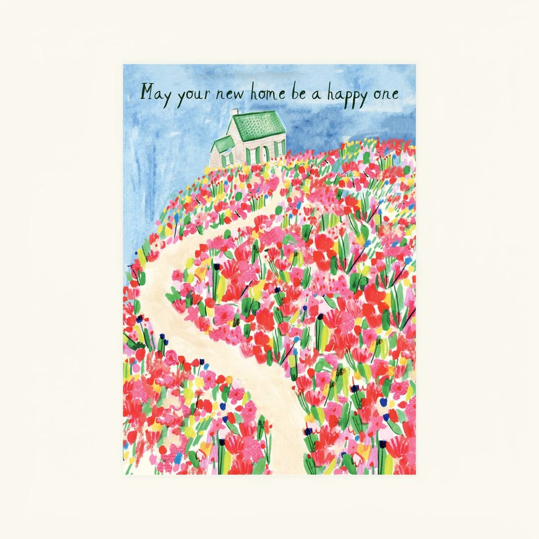 A watercolor-style art print featuring a winding cream path through a dense field of pink, red, and green flowers, leading to a small white house with a green roof. Handwritten text at the top reads, 'May your new home be a happy one.