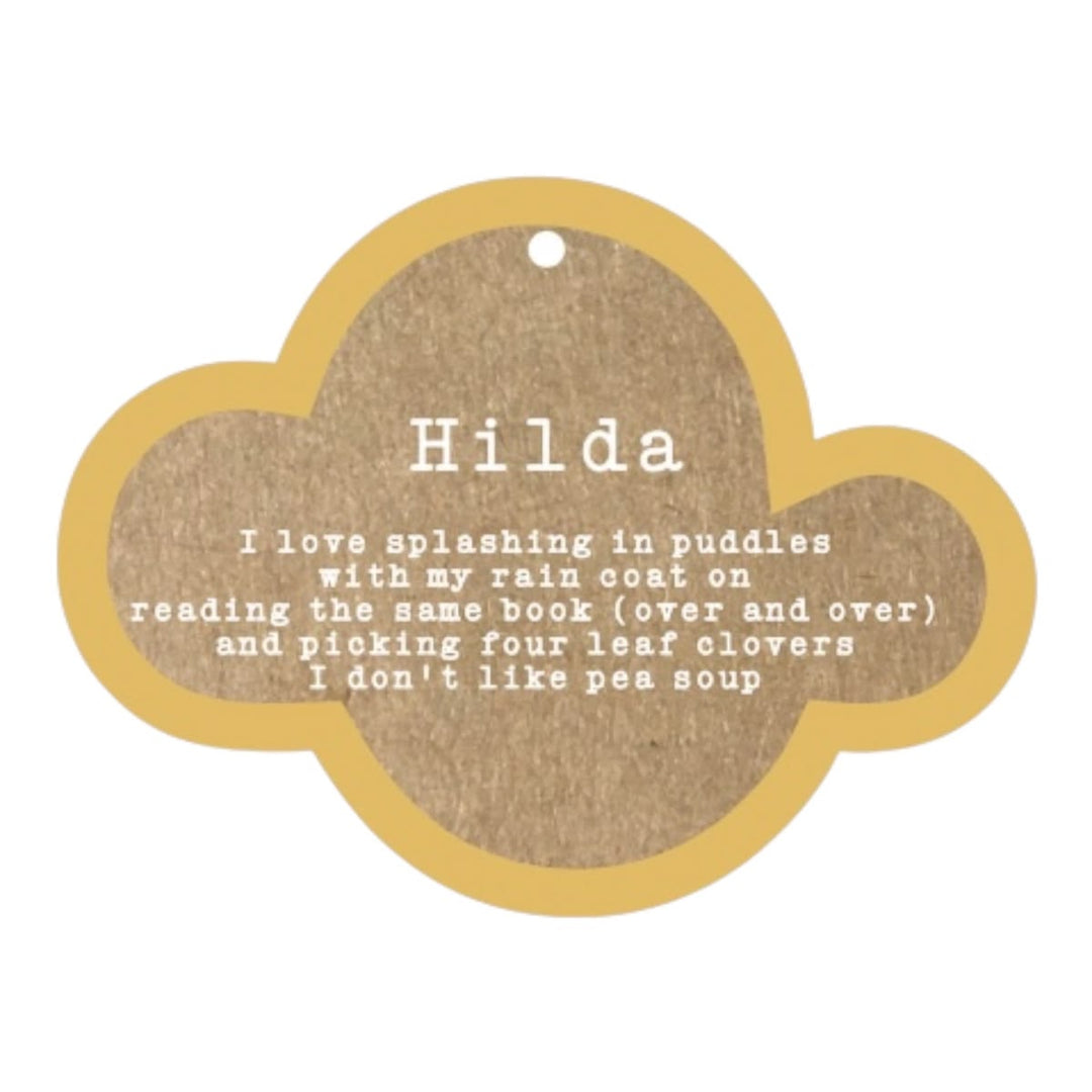A cloud-shaped wooden name plaque for a pet, featuring a natural brown wood grain center with white printed text and a light tan wood border. The name 'Hilda' is printed at the top, followed by a humorous pet quote about reading and pea soup.