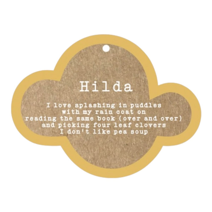 A cloud-shaped wooden name plaque for a pet, featuring a natural brown wood grain center with white printed text and a light tan wood border. The name 'Hilda' is printed at the top, followed by a humorous pet quote about reading and pea soup.