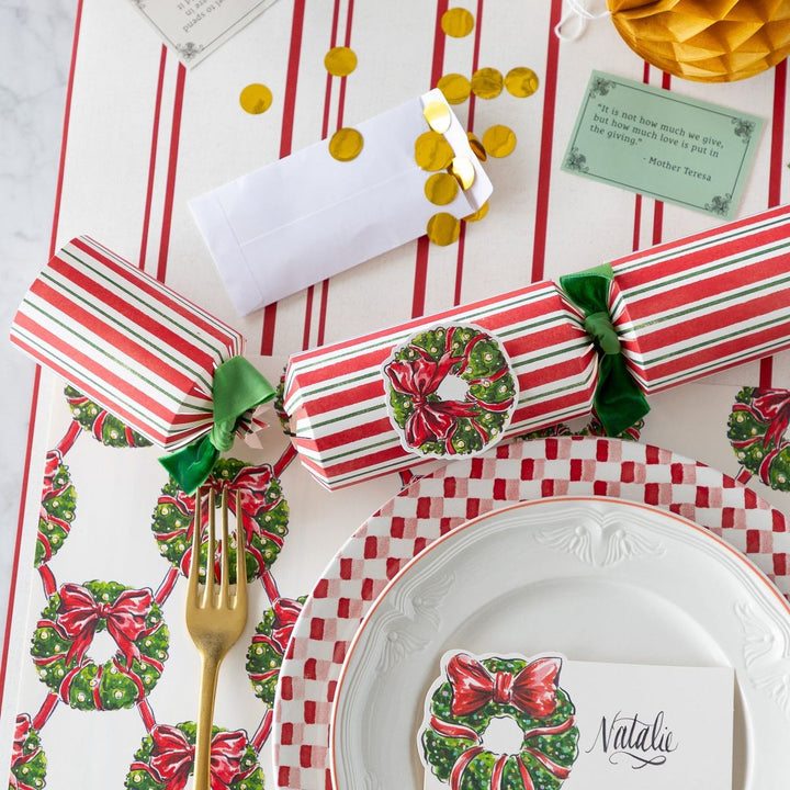 Christmas-themed table setting with crackers, napkins, and decorative elements on a red and white striped tablecloth.