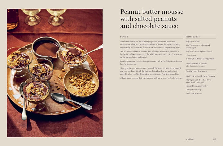 Peanut butter mousse with salted peanuts and chocolate sauce on a tray with spoons, on a wooden surface.