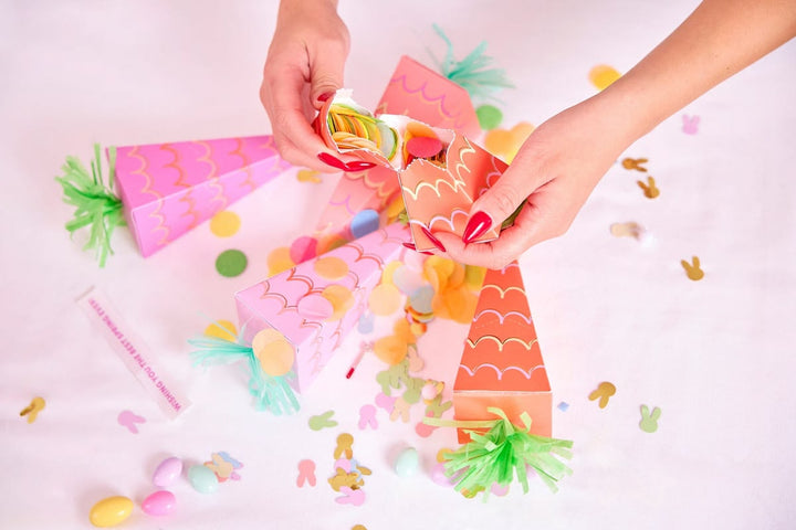 Colorful paper crafts shaped like carrots and other shapes on a light pink background.