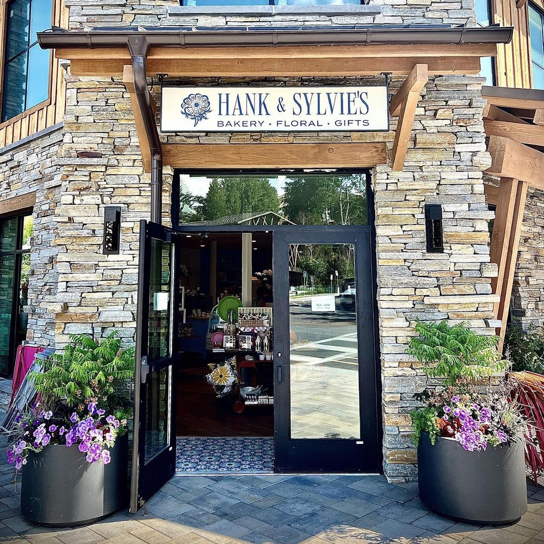 Storefront of Hank & Sylvie's Bakery, Floral, and Gifts with stone facade and open doors.