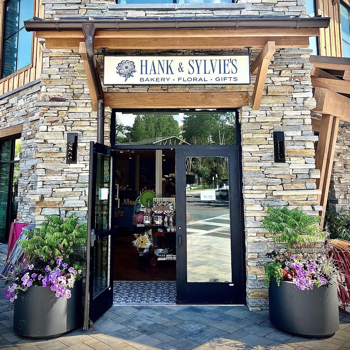 Storefront of Hank & Sylvie's Bakery, Floral, and Gifts with stone facade and open doors.