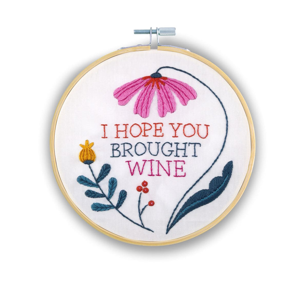 A circular embroidery hoop containing a floral design and the embroidered text 'I HOPE YOU BROUGHT WINE' on white fabric, photographed against a plain white background.