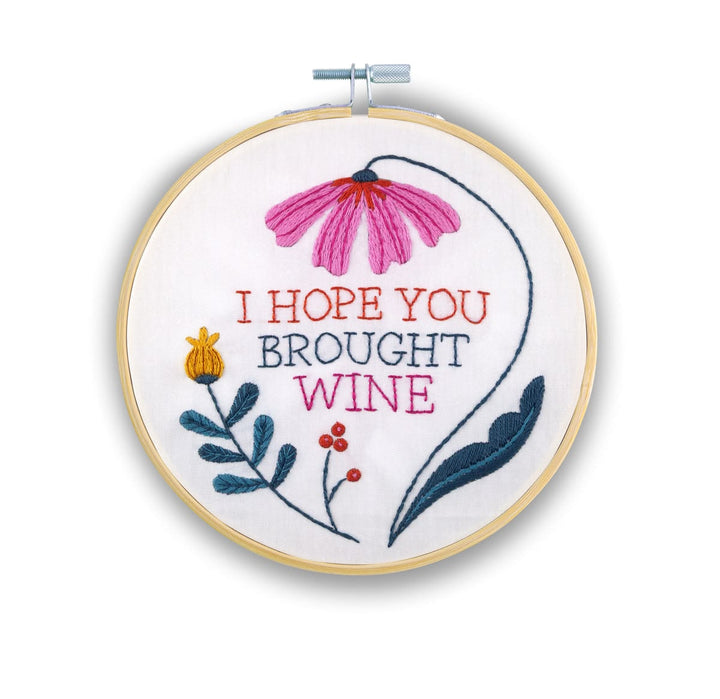A circular embroidery hoop containing a floral design and the embroidered text 'I HOPE YOU BROUGHT WINE' on white fabric, photographed against a plain white background.