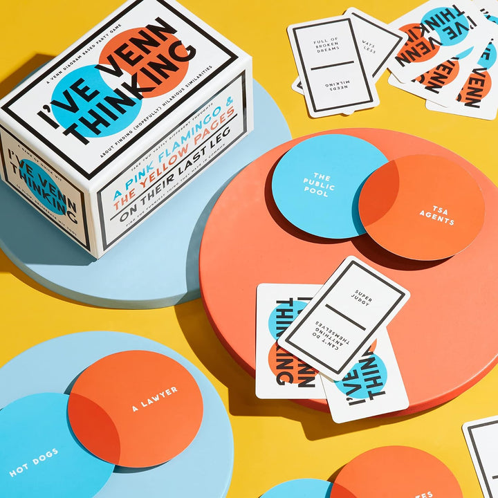 Board game components including a box, cards, and circular markers on a yellow background