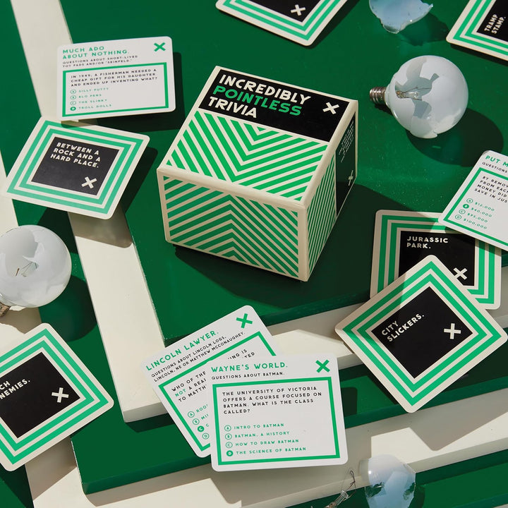 Hexagonal box labeled 'Incredibly Pointless Trivia' surrounded by green and black cards on a green surface.