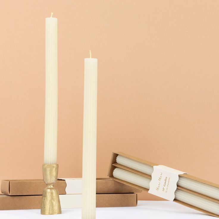 Two tall white candles with gold holders on a beige background