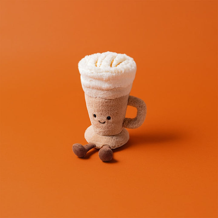 Plush toy resembling a cup of coffee with a smiley face on an orange background