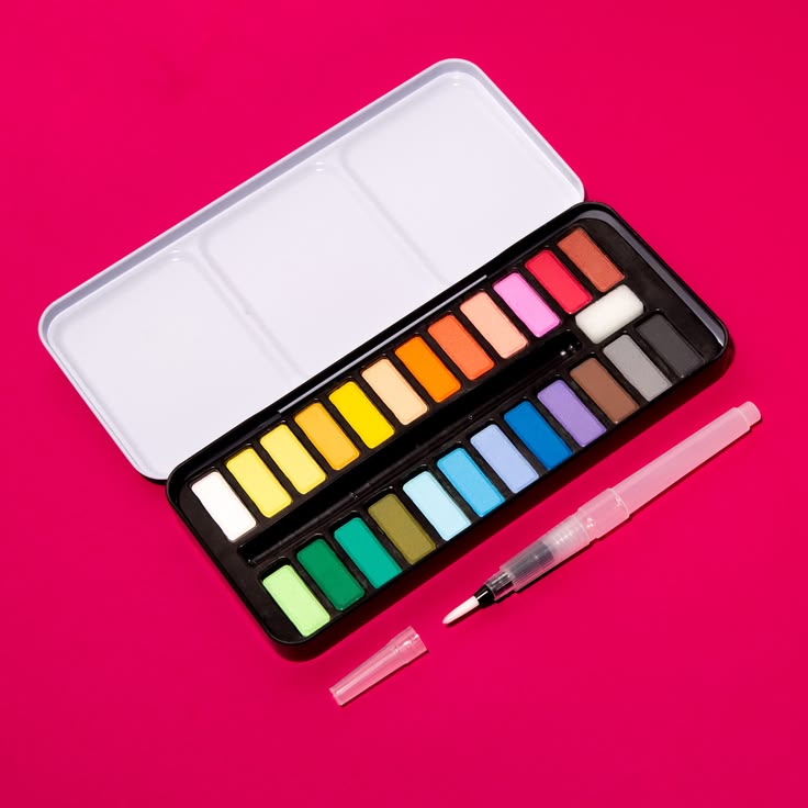 Watercolor paint set with a brush on a pink background