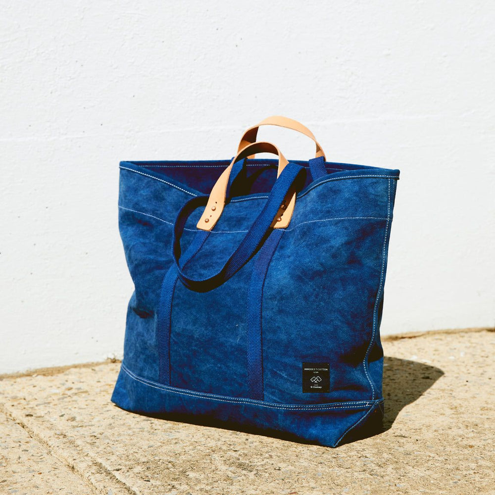 Blue tote bag with leather handles on a concrete surface