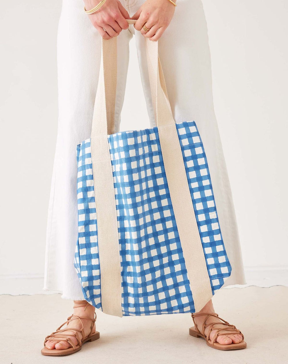 Person holding a blue and white checkered bag with beige straps on a plain background