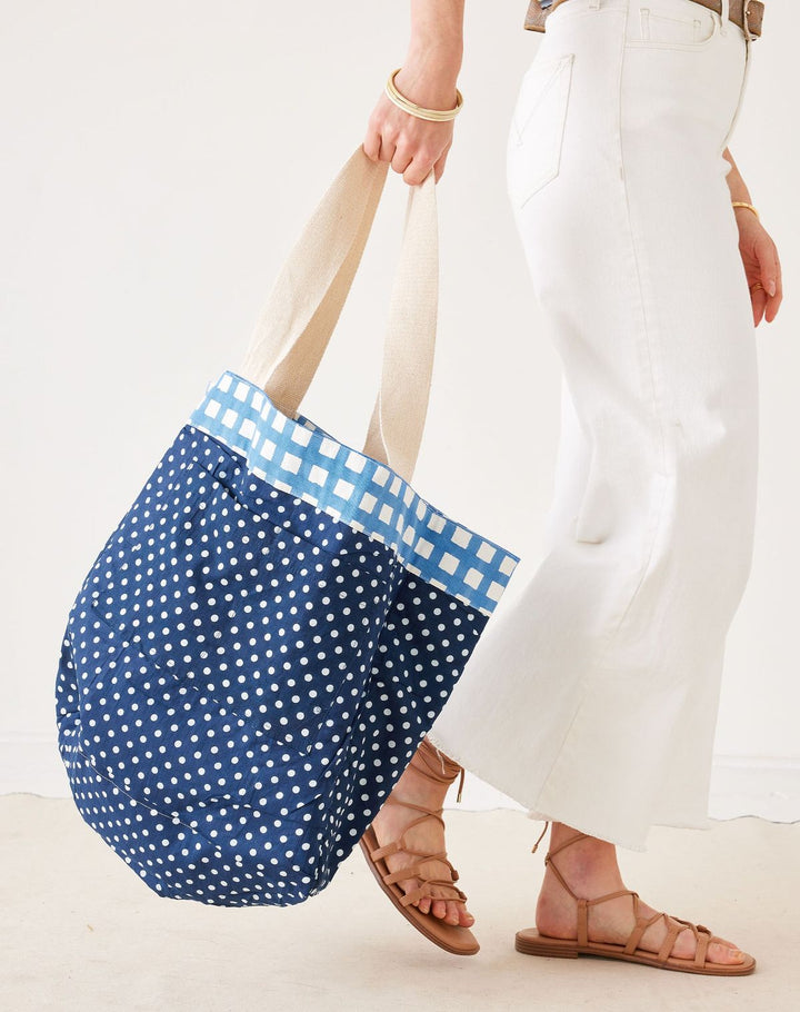 Person holding a blue polka dot bag with a checkered trim against a white background