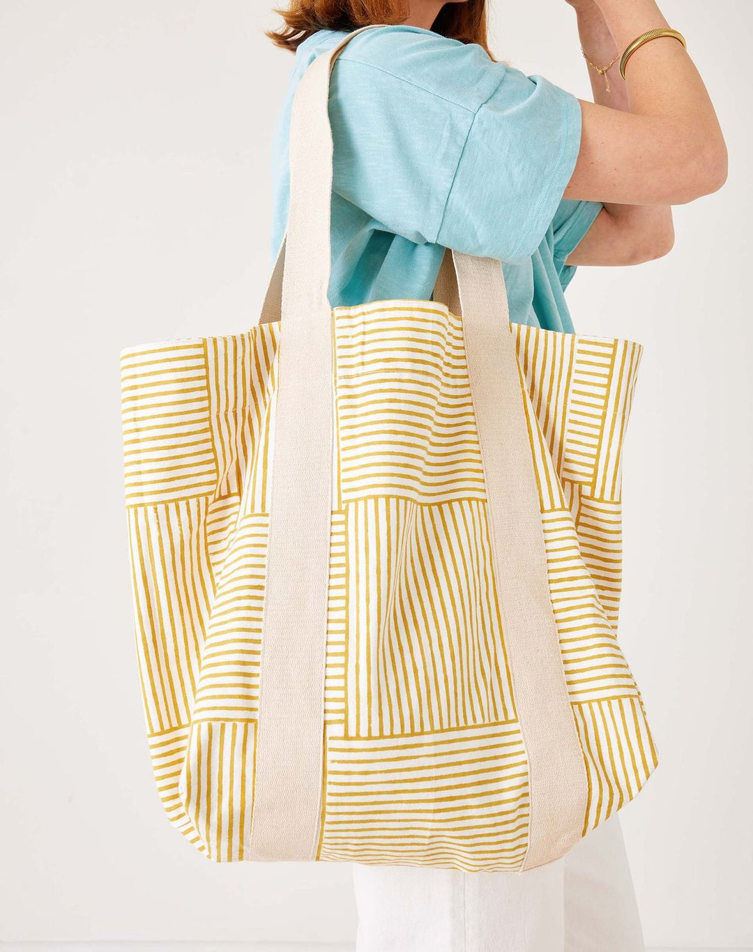 Person holding a yellow and white patterned tote bag against a plain background