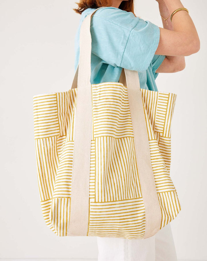 Person holding a yellow and white patterned tote bag against a plain background