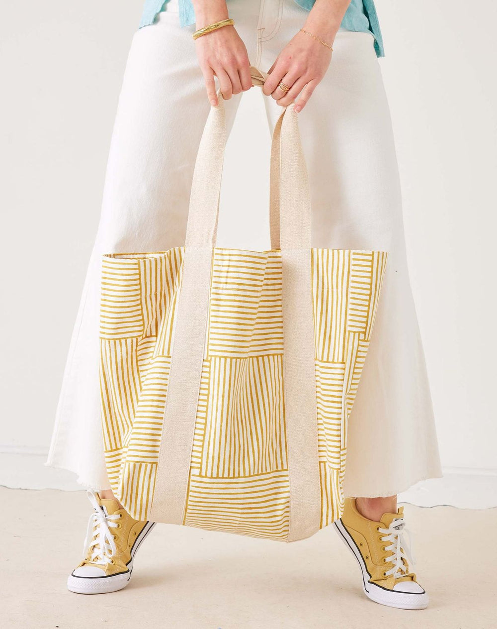 Person holding a tote bag with yellow geometric pattern on a plain background