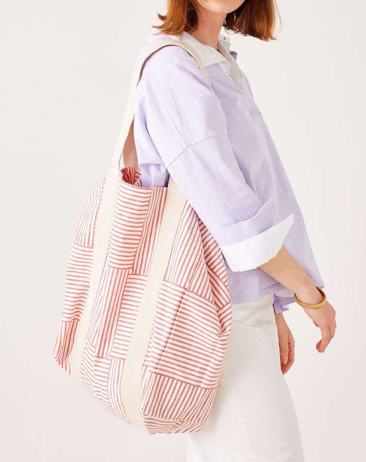 Person wearing a light purple shirt and white pants with a red and beige striped bag on a white background