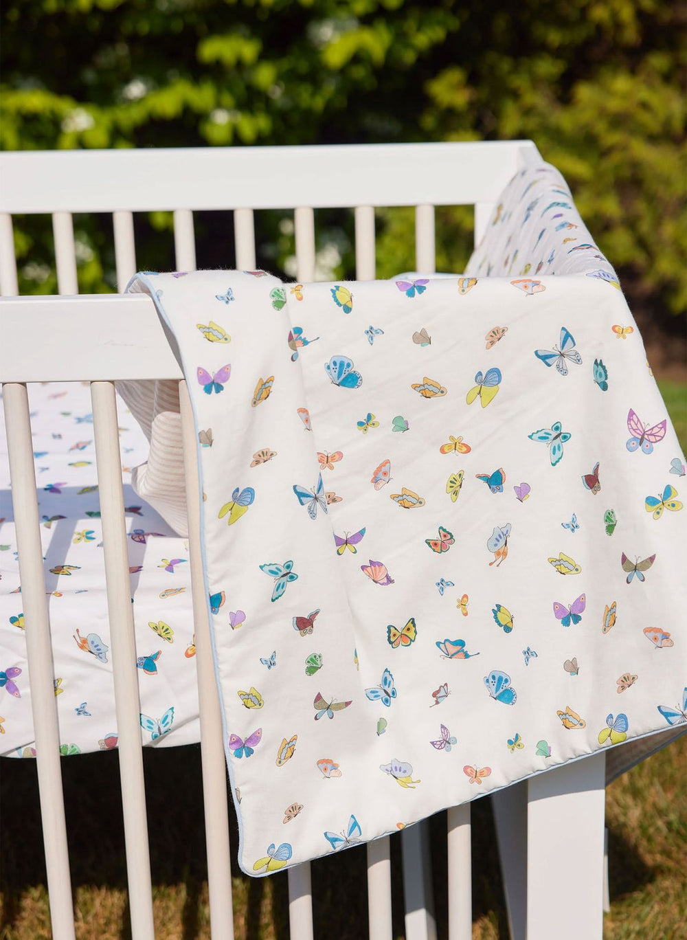 Butterfly-patterned blanket draped over a white crib outdoors.