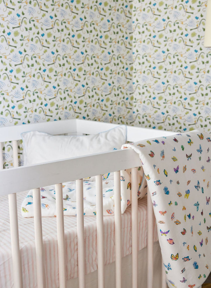 Crib with colorful butterfly-patterned crib sheet against a floral wallpaper background