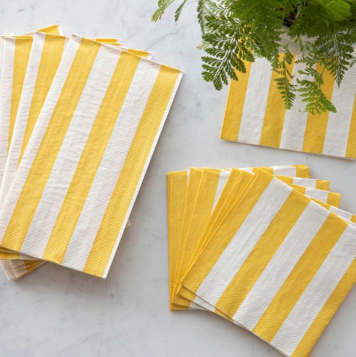 Yellow and white striped napkins on a marble surface with greenery.