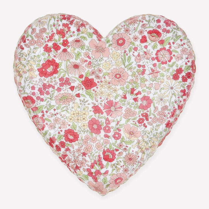 A heart-shaped decorative pillow featuring a dense, all-over floral print with pink, red, and yellow flowers on a white background, set against a solid light gray backdrop.