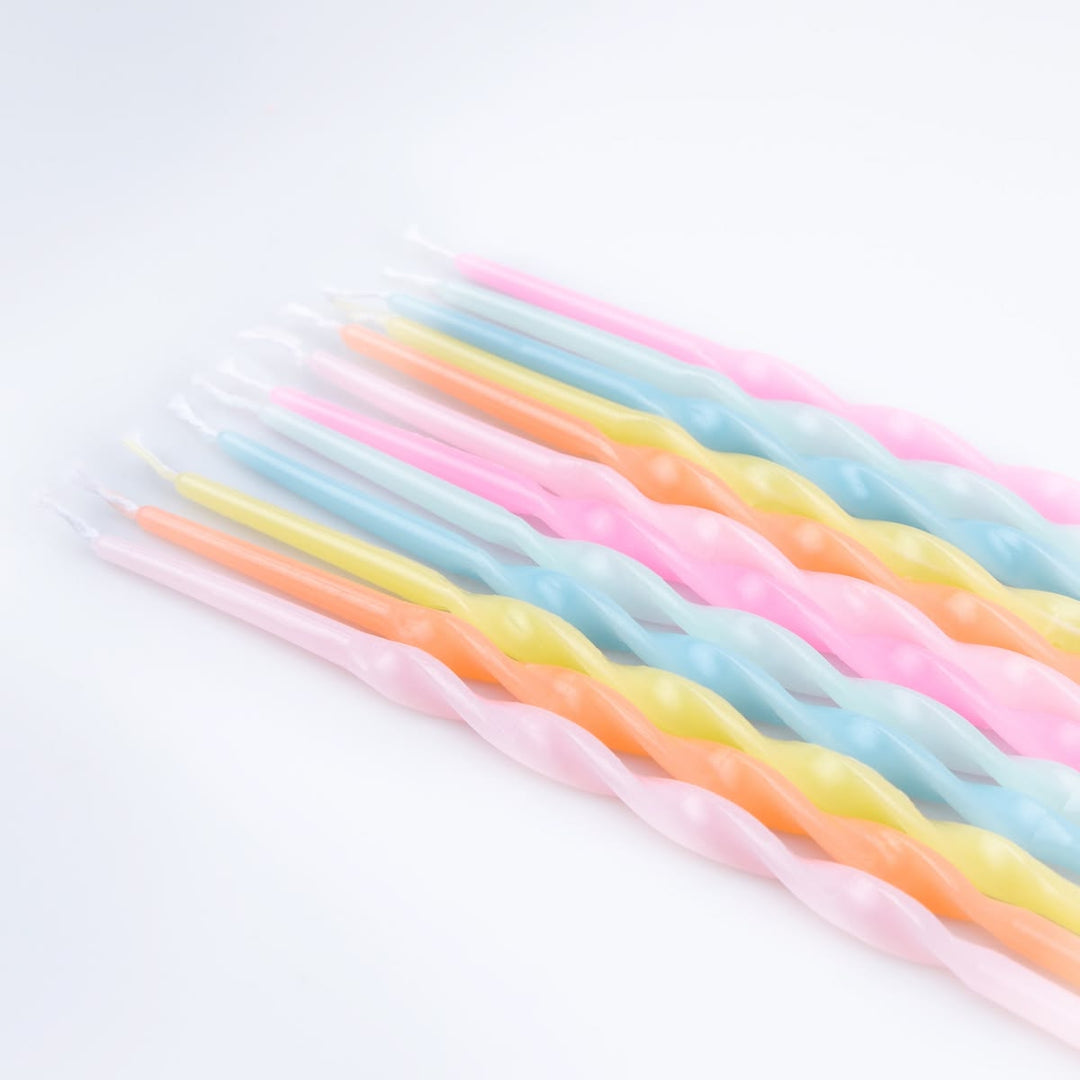A set of twisted birthday candles in pastel colors, including pink, light blue, yellow, and orange, arranged diagonally on a white background.