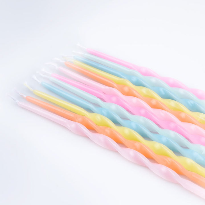 A set of twisted birthday candles in pastel colors, including pink, light blue, yellow, and orange, arranged diagonally on a white background.